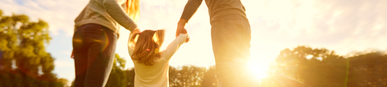 A woman and man holding a little girls hand outside in a park or yard